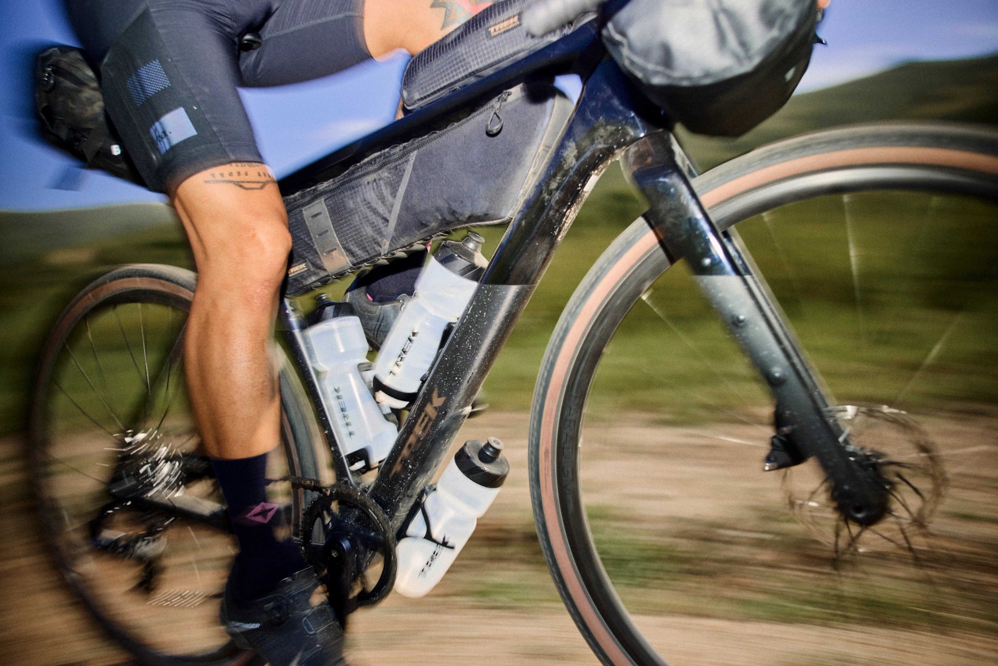 Fahrradfahrer auf einem Trek Checkpoint Gravel-Bike mit Gepäcktaschen und Trinkflaschen auf einer Schotterstraße.