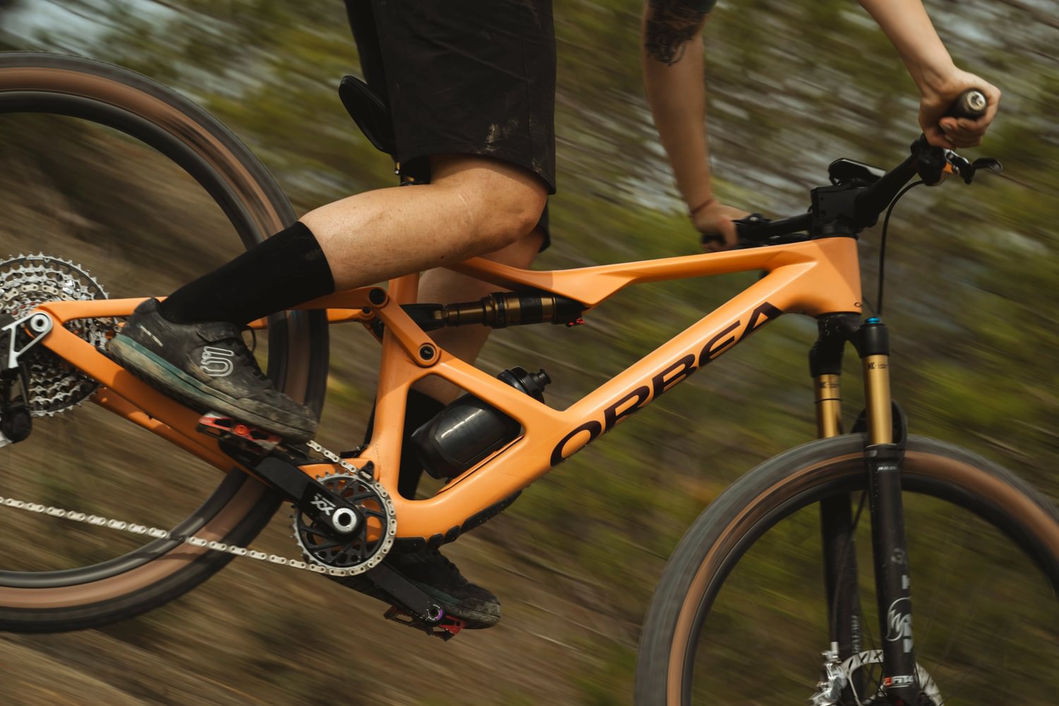 Orbea Mountainbike in Aktion, orangefarben, kurvige Trails, sportlicher Fahrer. Ideal für Abenteuer und Outdoor-Enthusiasten.