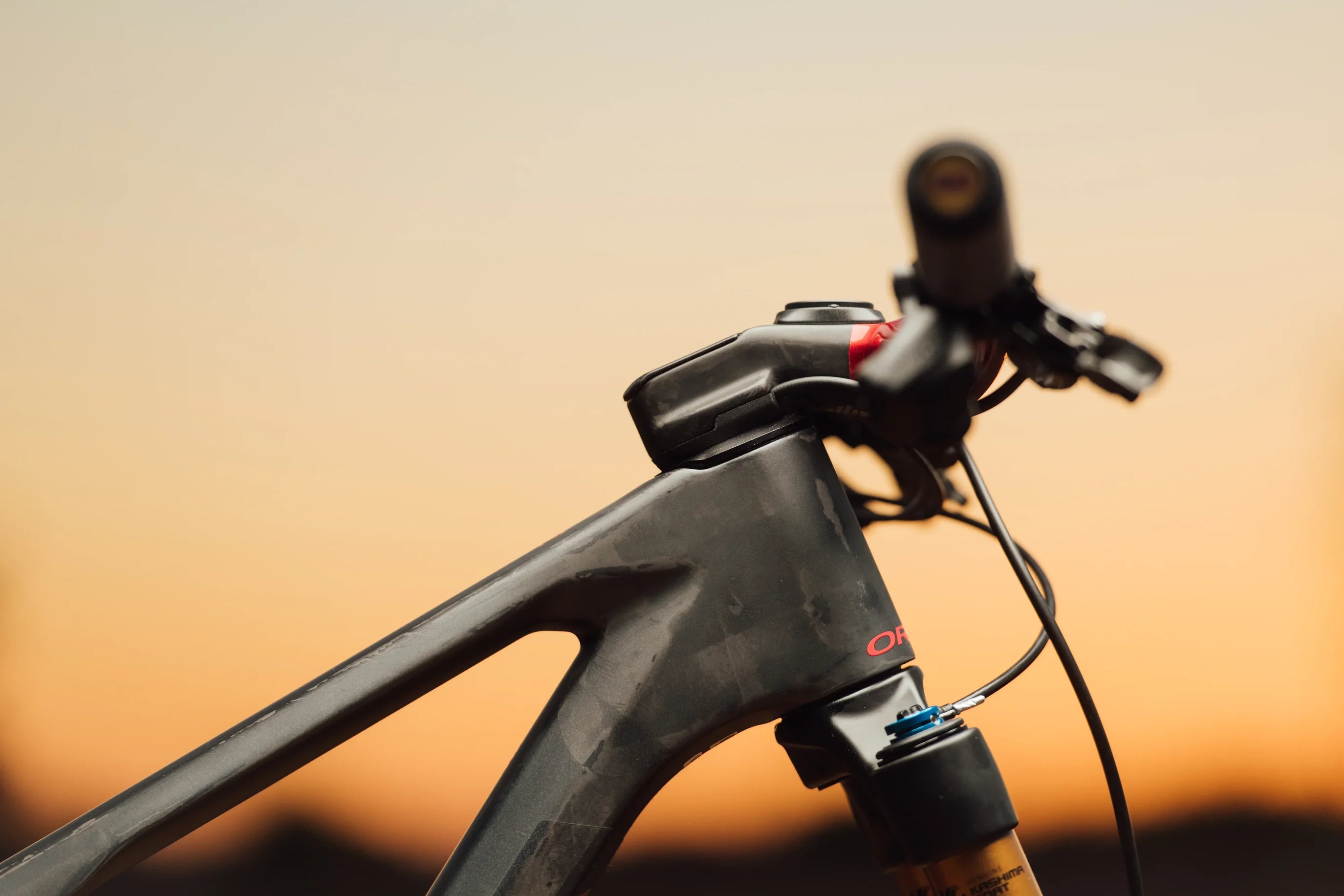 Nahaufnahme eines schwarzen Carbon-Mountainbike Rahmens und Lenkers, geeignet für Geländefahrten bei Sonnenuntergang.