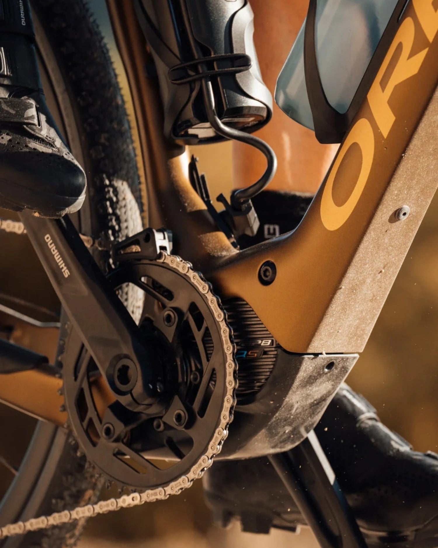 Nahaufnahme eines goldenen Orbea E-Bikes mit Shimano-Antrieb, Kette, Pedal und Wasserflasche für den Outdoor-Einsatz.