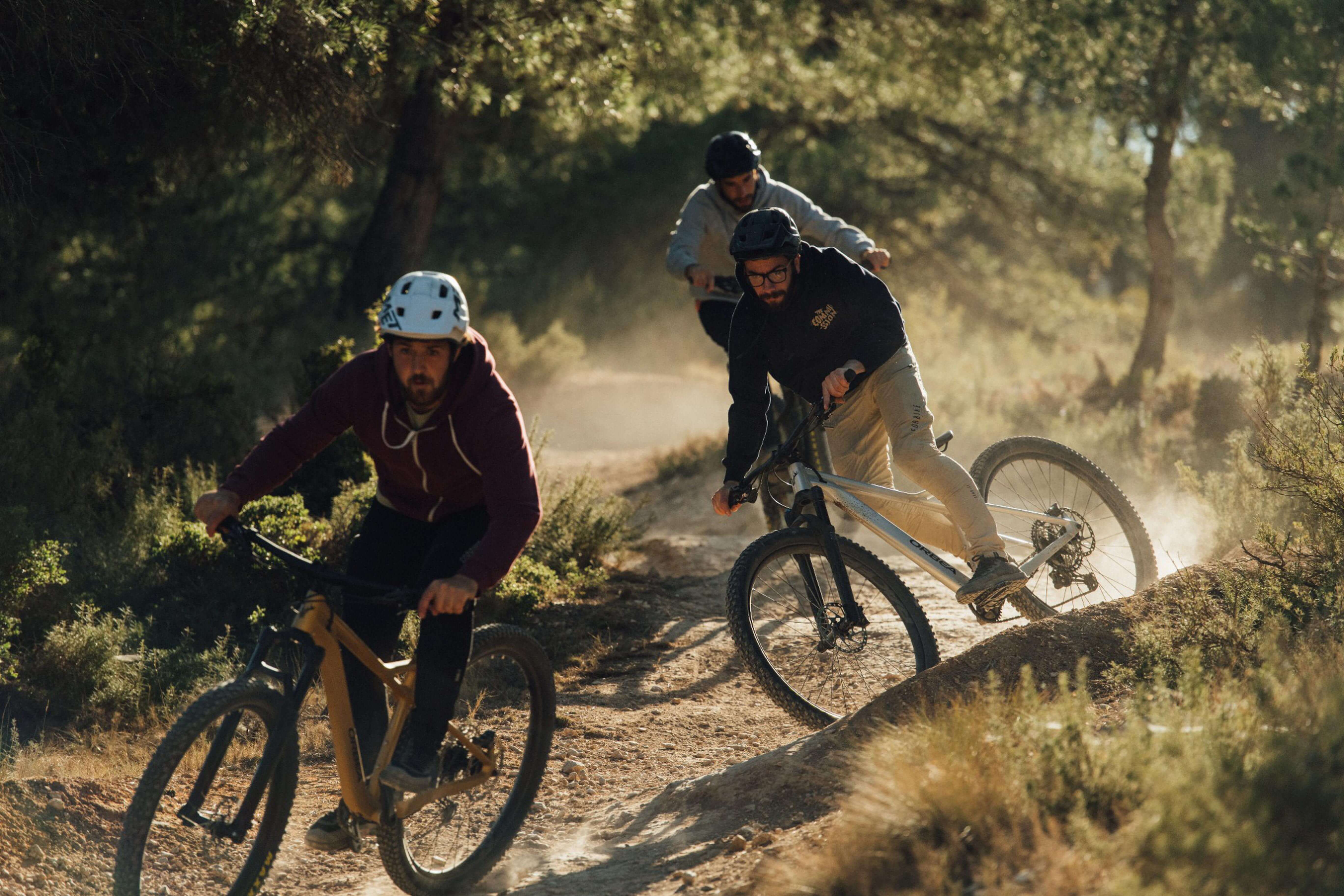 Drei Mountainbiker fahren durch Waldstrecke, zwei mit Orbea-Fahrrädern, ideal für Offroad-Abenteuer.