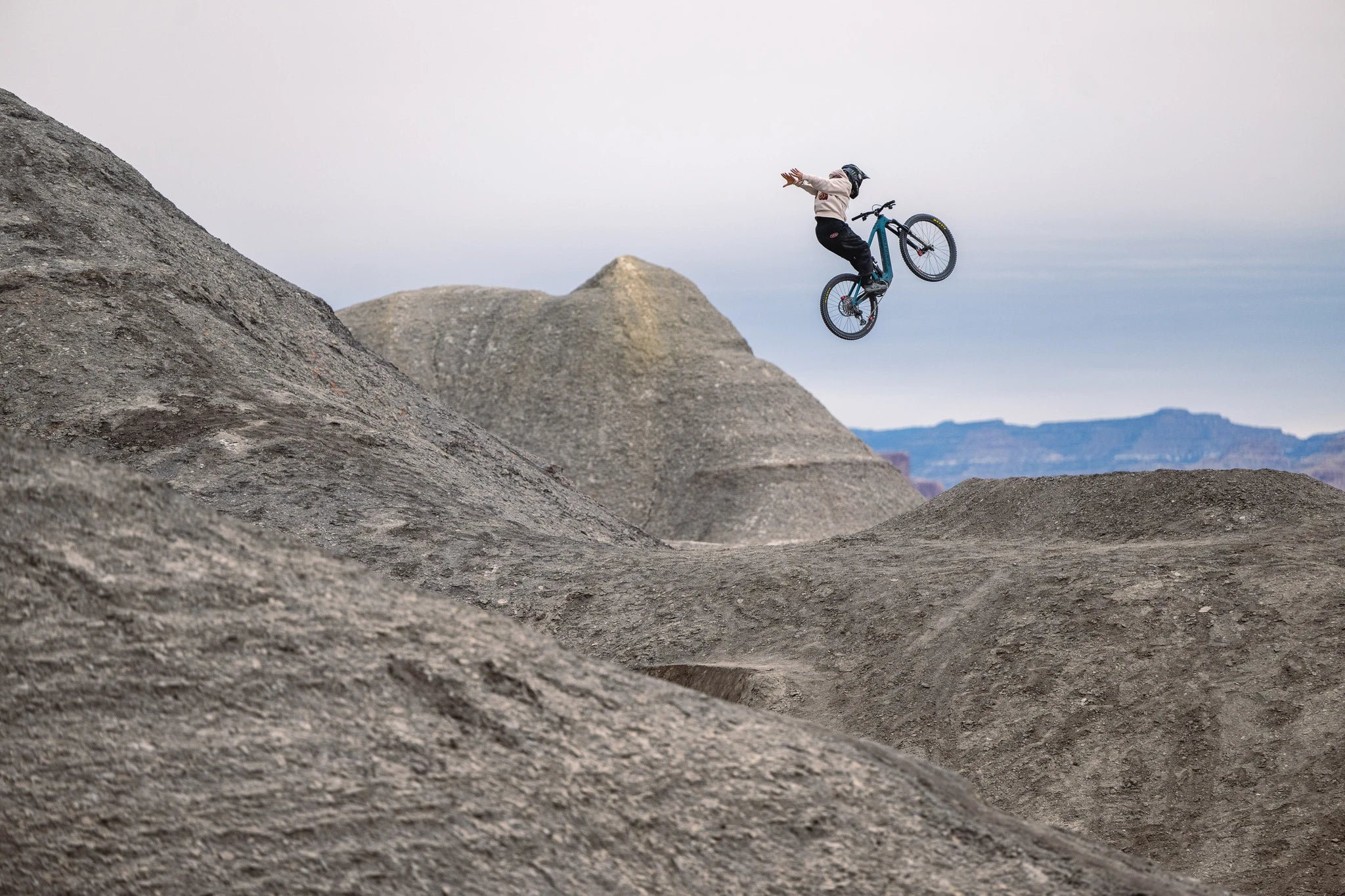 Mountainbiker macht Stunt in felsiger Landschaft mit Santa Cruz Bullit E-Mountainbike vor bergigem Hintergrund.