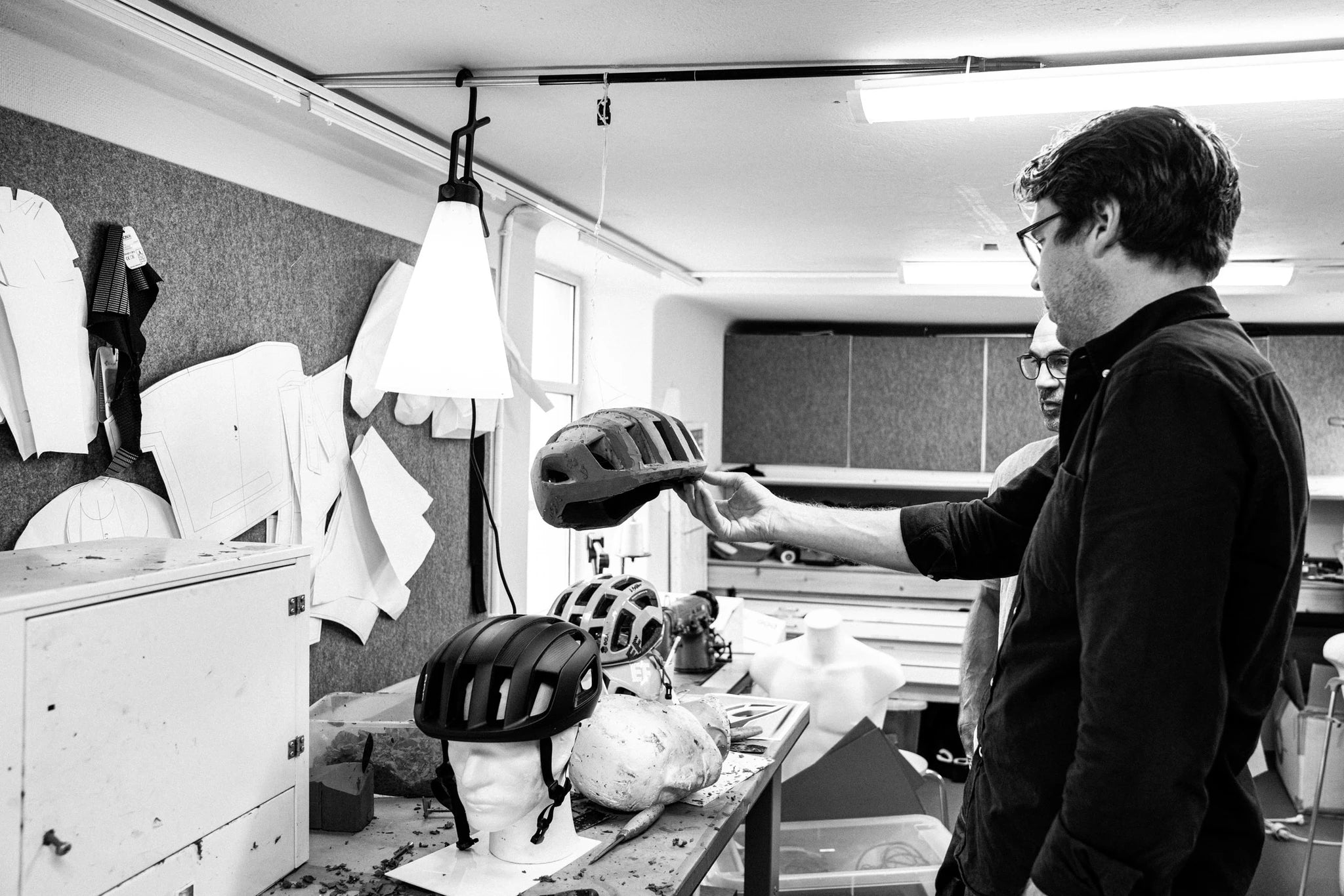Zwei Männer begutachten einen Fahrradhelm-Prototyp, umgeben von Designmaterialien in einem Atelier.