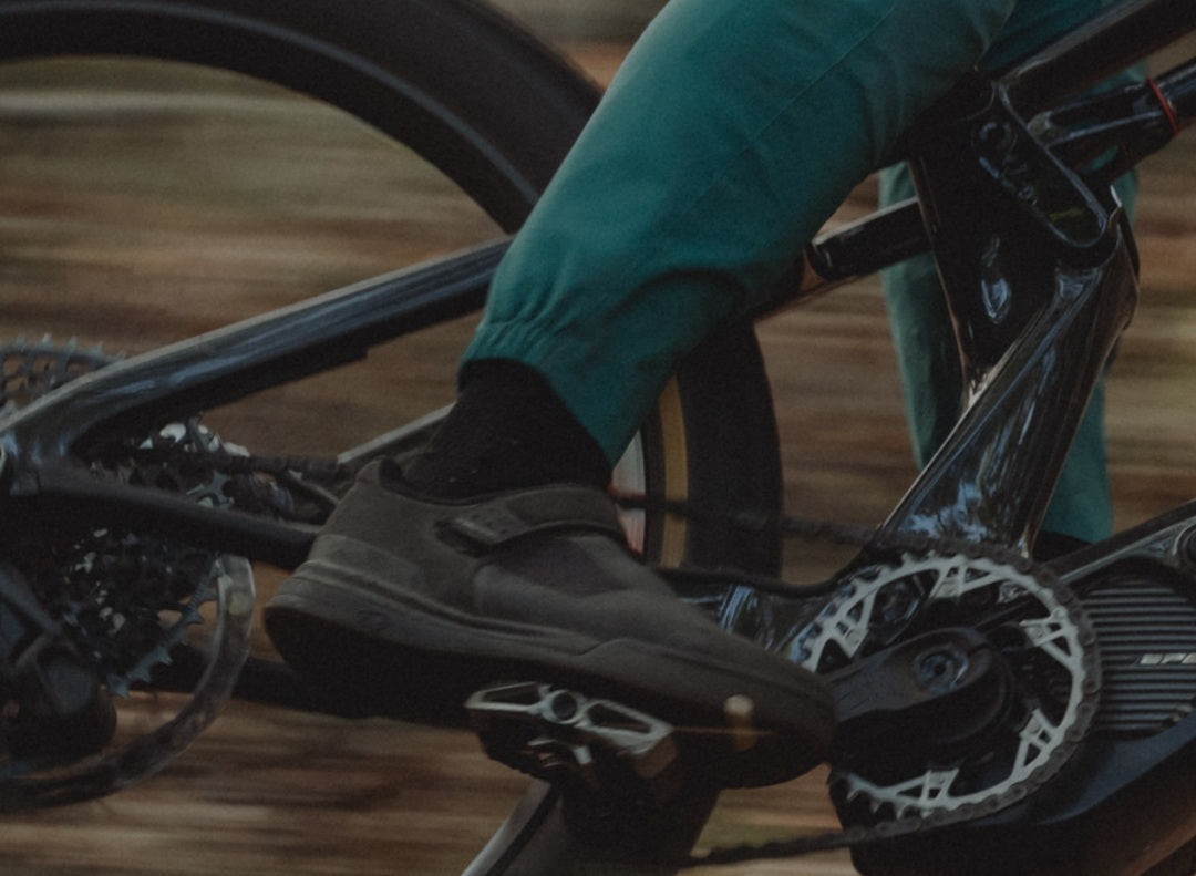 Radfahrer mit grüner Hose tritt in Fahrradpedal. Nahaufnahme von Pedal und Schuh, im Hintergrund Unscharfe Bewegung.