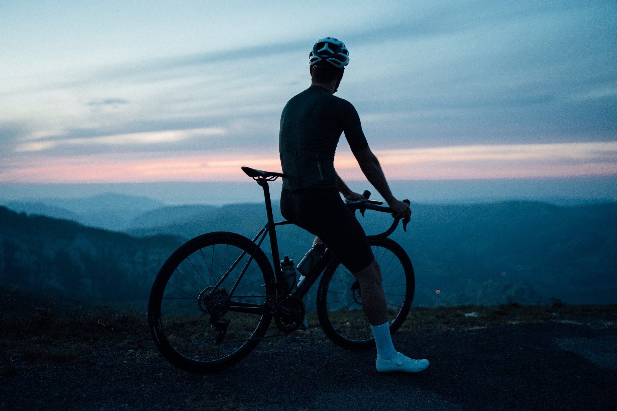 Radfahrer auf einem Orbea Orca Rennrad mit Helm vor Bergpanorama in der Dämmerung.