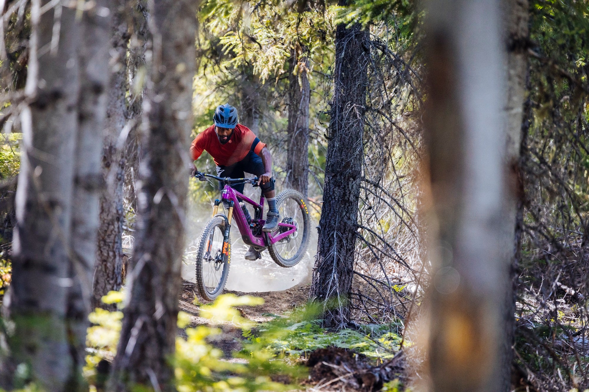 Person auf Santa Cruz E-MTB fährt durch Wald, hebt ab. Zielgruppe: Mountainbike-Enthusiasten.