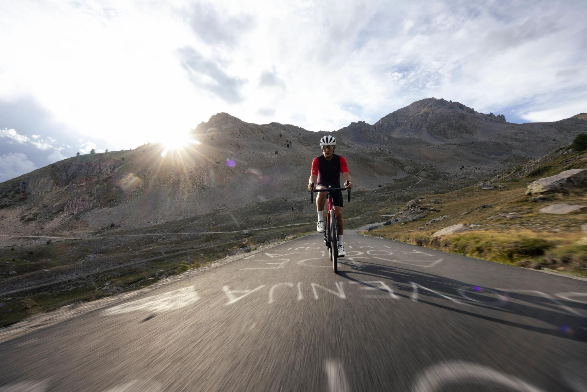 Radfahrer auf Trek Domane Rennrad, rote Kleidung, Helm, bergige Straße bei Sonnenaufgang.