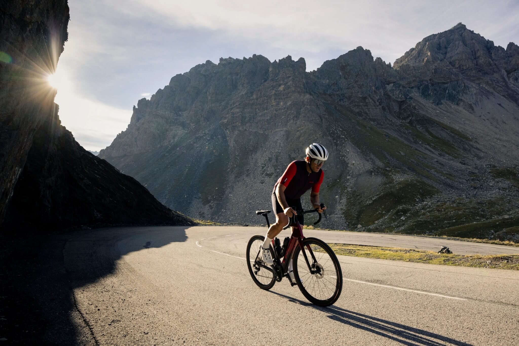 Radfahrer auf einem Trek Domane Rennrad, bergauf auf einer kurvenreichen Bergstraße vor einer felsigen Bergkulisse.