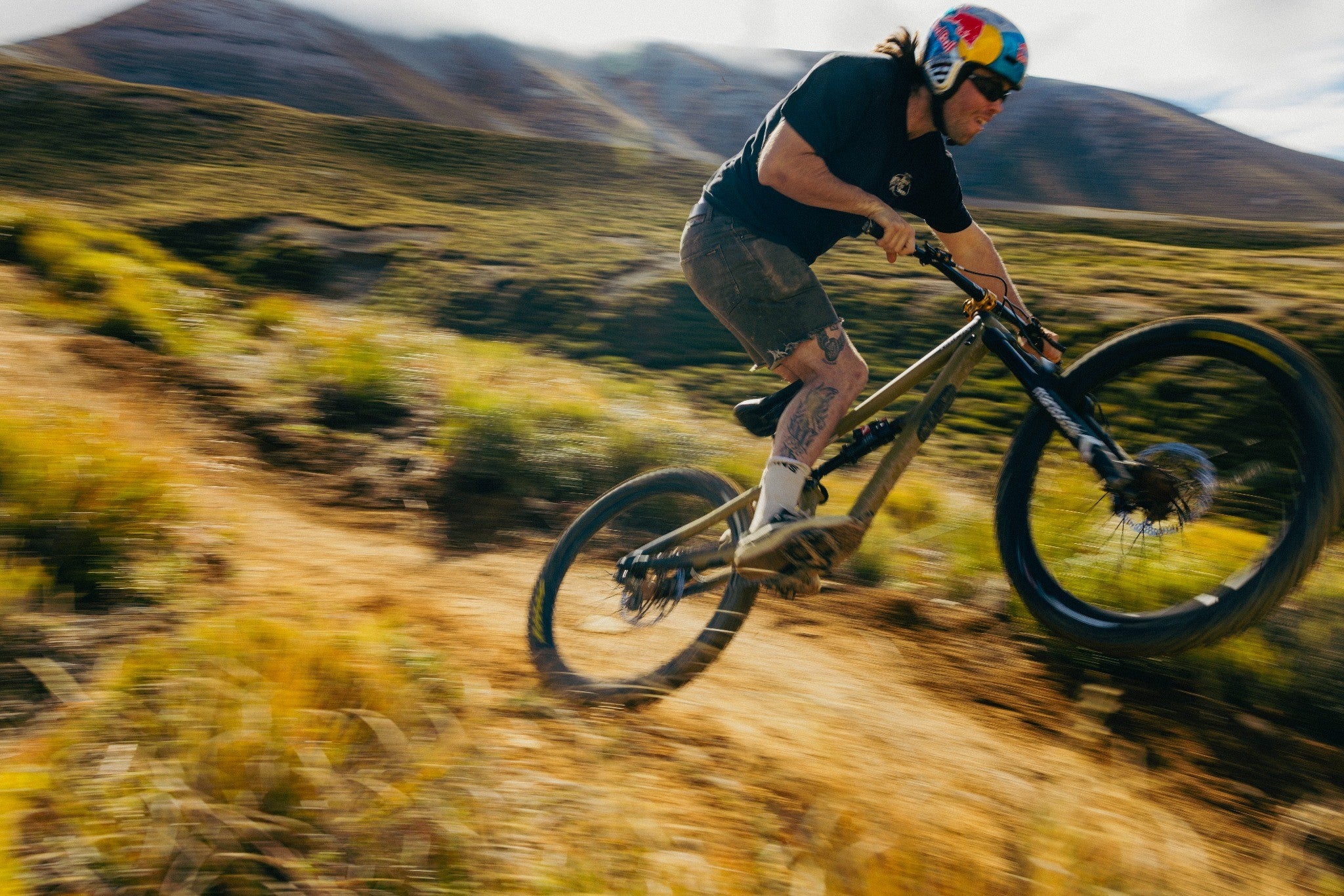 Person fährt schnell mit Mountainbike auf einem Schotterweg in bergiger Landschaft.