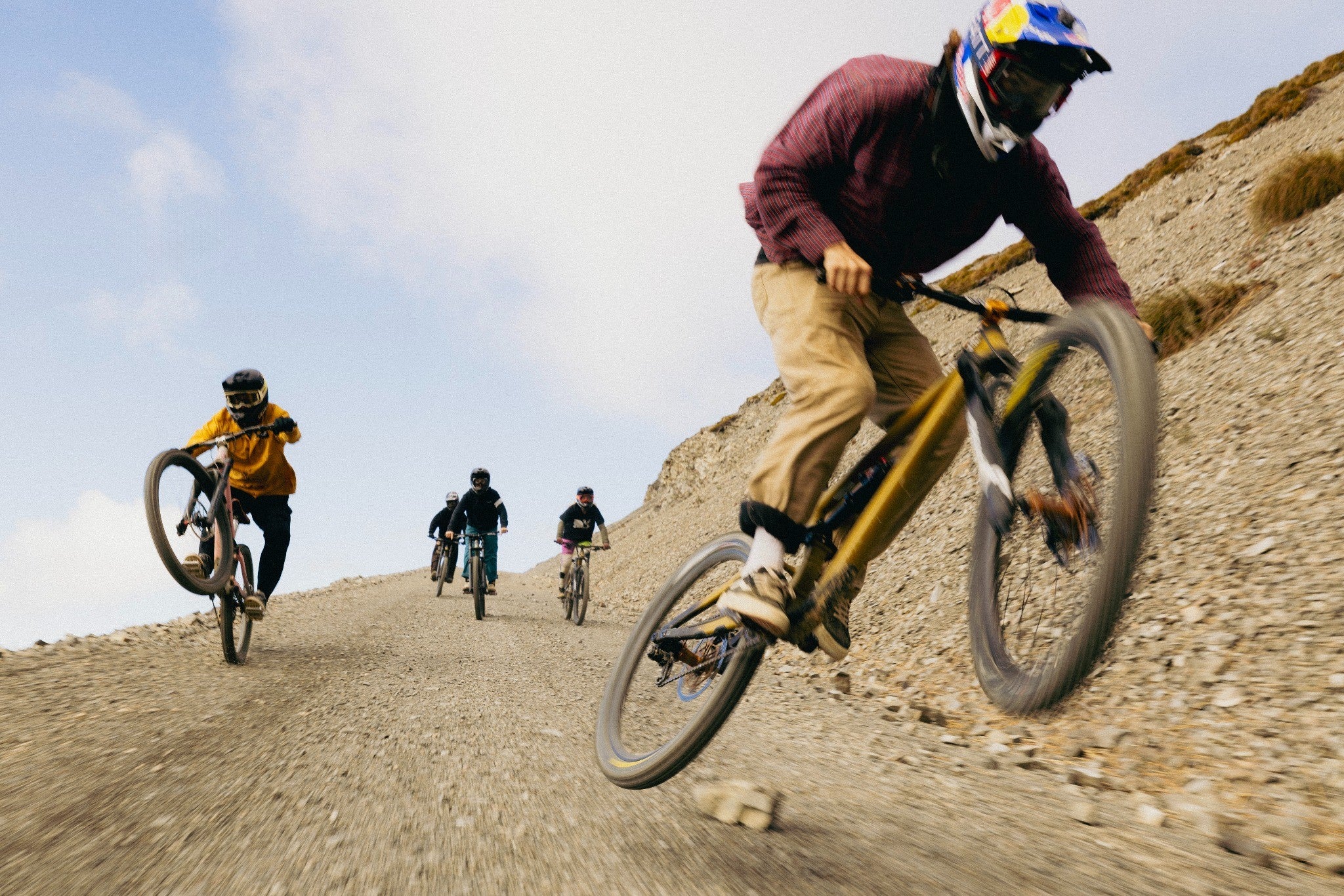 Mountainbiker fahren eine steinige Abfahrt hinunter, einer macht einen Stunt. Darstellung dynamischen Fahrverhaltens.