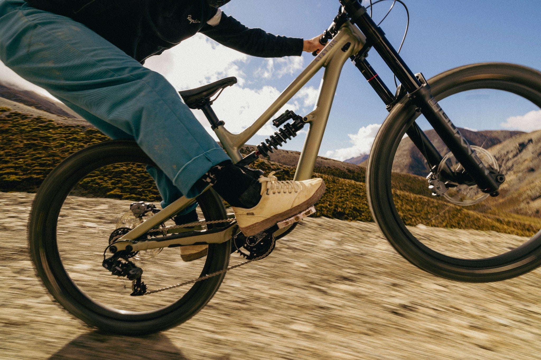 Mountainbike Specialized Status bei Abfahrt im Gelände, Fahrer in blauer Hose und Sneakern zeigt dynamische Aktion.