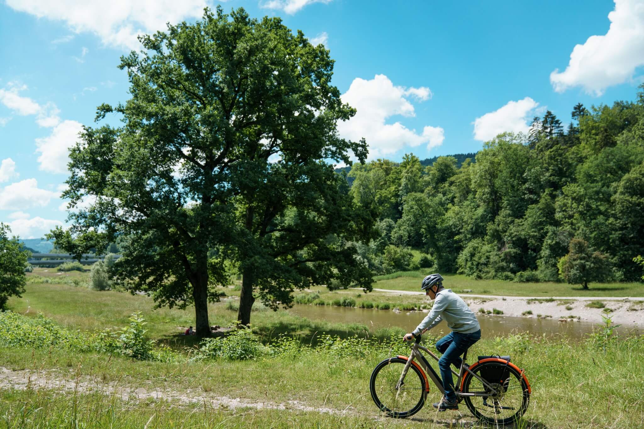 Person fährt ein BMC E-Bike auf einem Pfad in einer grünen, ländlichen Umgebung bei sonnigem Wetter.