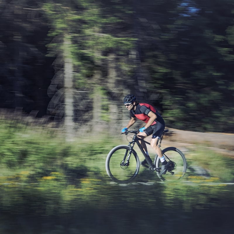 Radfahrer in rotem Trikot auf einem Mountainbike im Wald, Collection: cube-elite, schnelle Bewegung dargestellt.