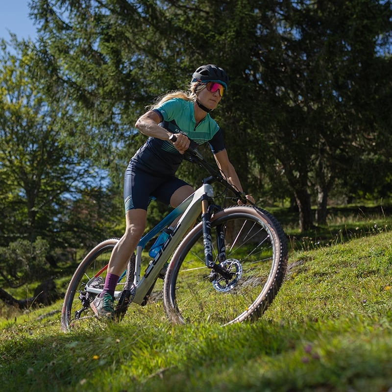 Frau fährt im Wald auf einem Cube Elite Mountainbike bergab.