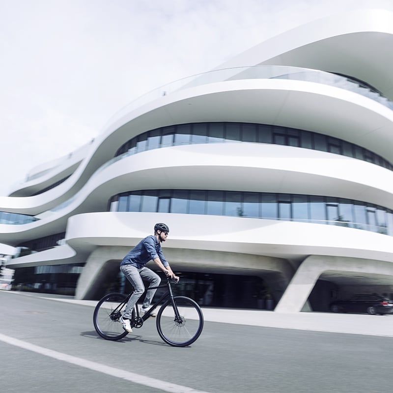 Person auf modernem Fahrrad vor futuristischem Gebäude. Ideal für urbane Pendler. Markennamen nicht erkennbar.