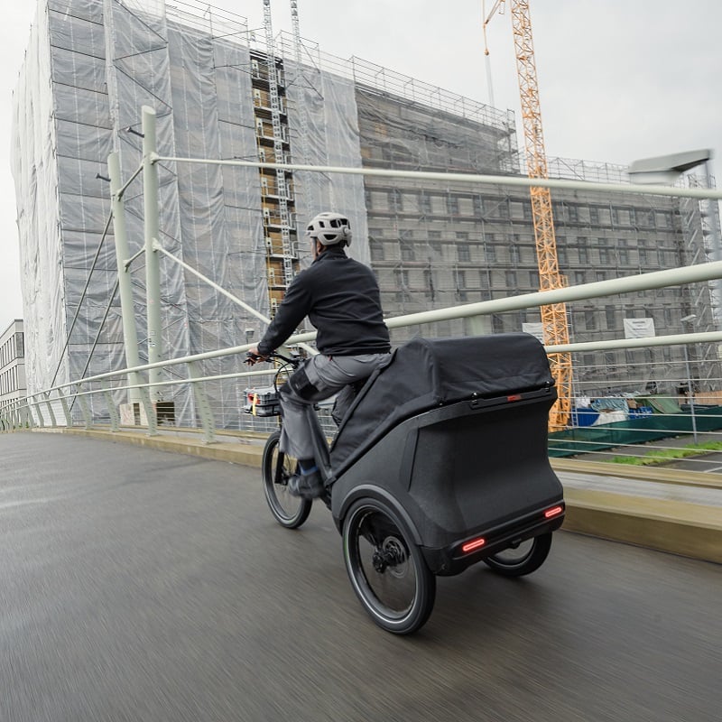 Person auf einem dreirädrigen Lastenfahrrad auf Brücke, urbane Umgebung. Modell: Cube Trike Hybrid.