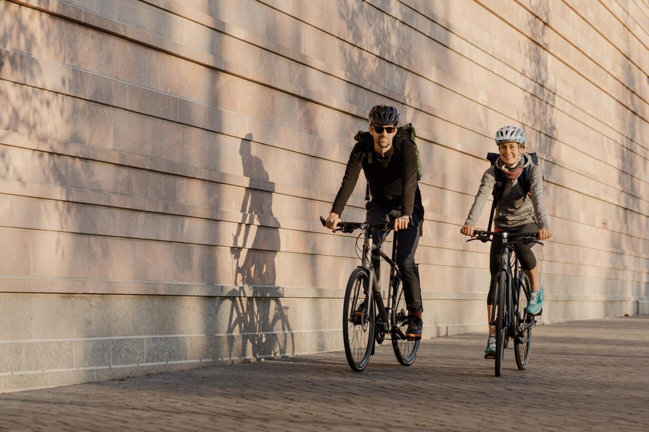 Zwei Personen auf Specialized-Fahrrädern fahren in urbaner Umgebung, tragen Helme und Freizeitkleidung.