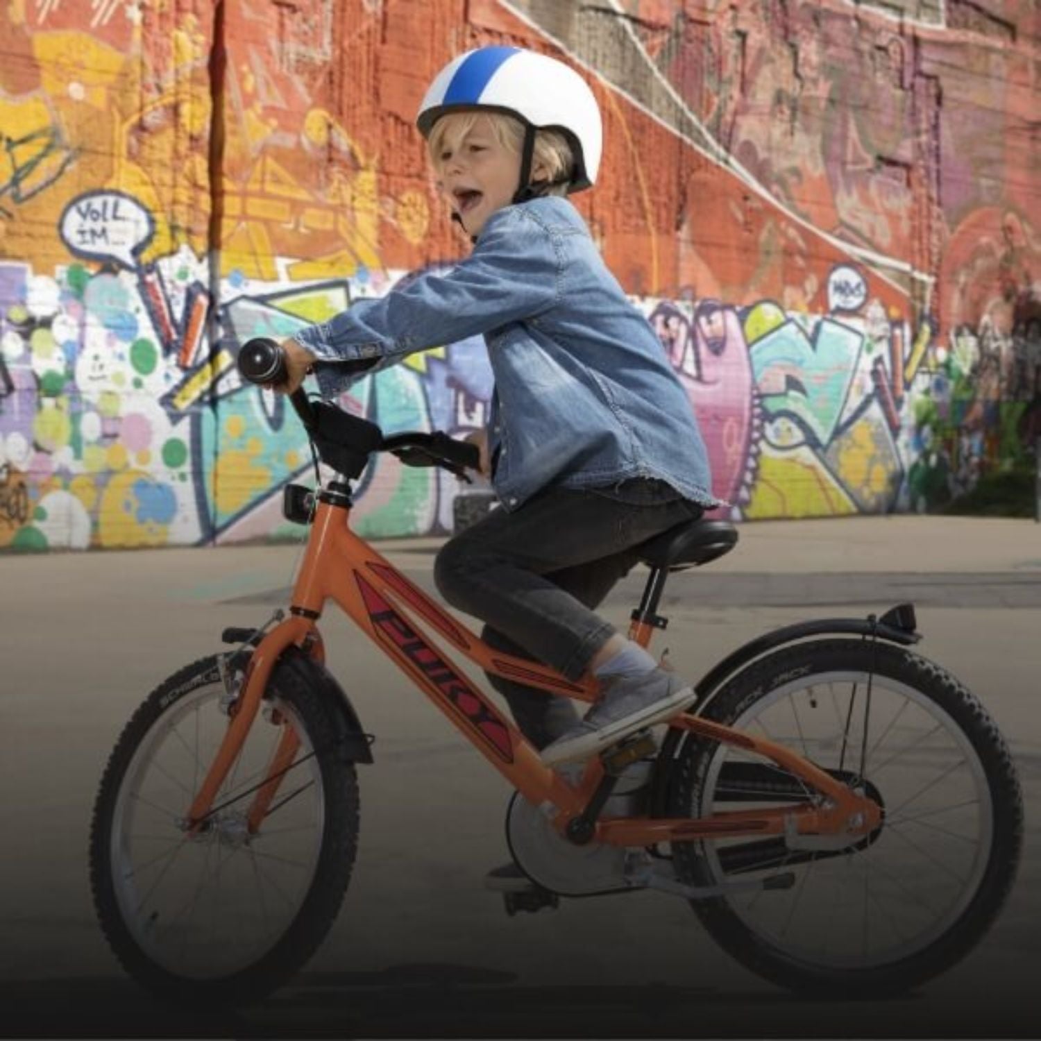 Kind auf orangefarbenem Fahrrad mit Helm vor bunter Graffiti-Wand. Fahrradsport für Kinder.