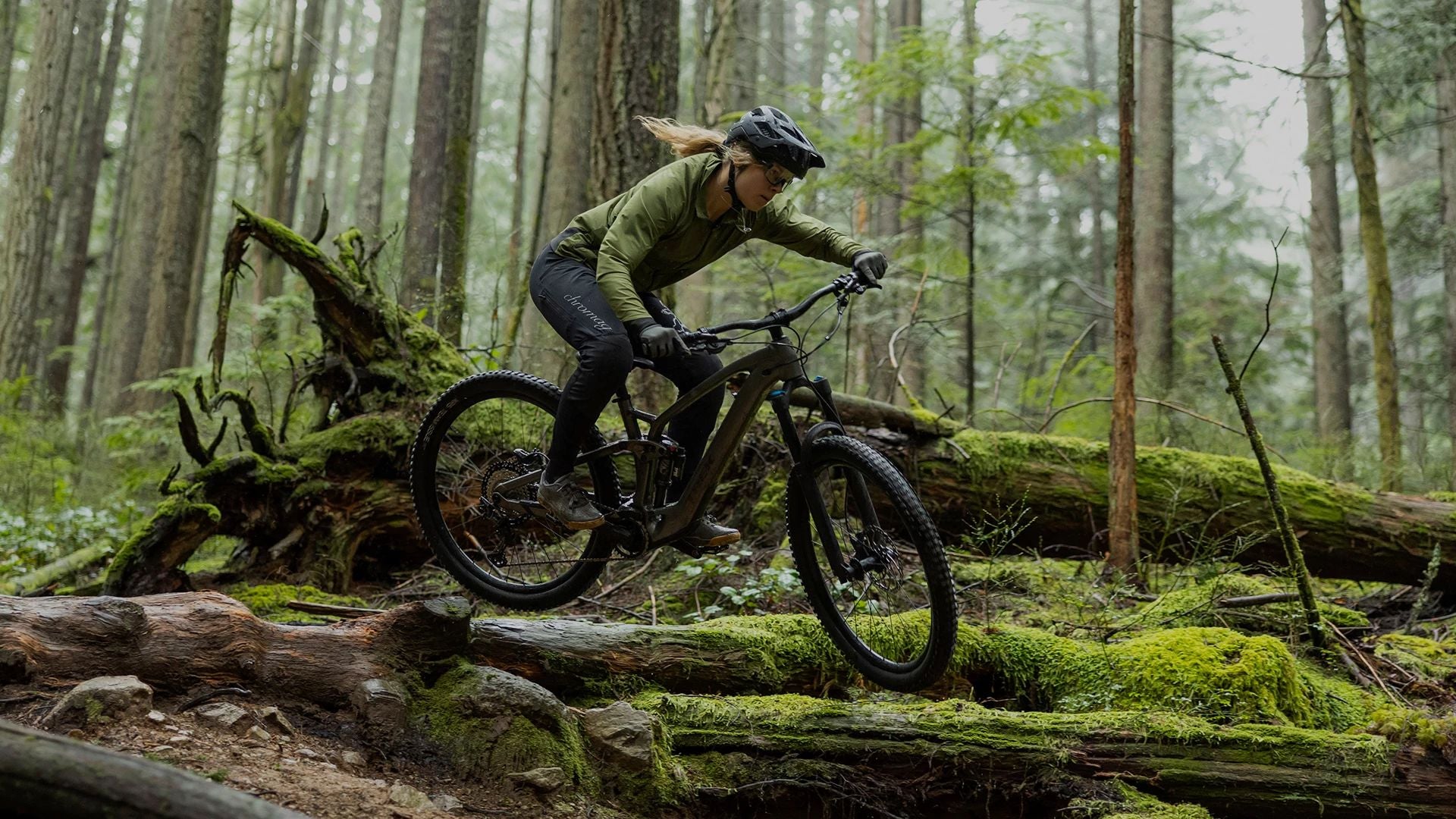 Person fährt ein Trek E-Mountainbike im Wald über einen mit Moos bedeckten Trail.
