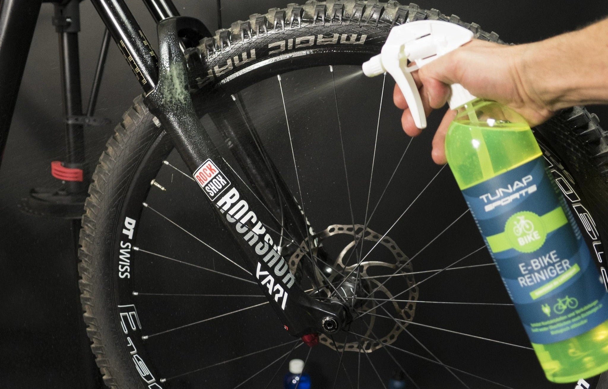 Sprühflasche mit TUNAP SPORTS E-Bike Reiniger vor einem Mountainbike-Rad mit RockShox Gabel.