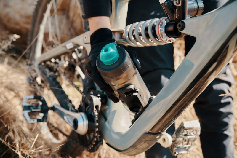Mountainbike mit Federung und Fahrradflasche in Halterung; Person in Fahrradausrüstung beim Aufsetzen der Flasche.
