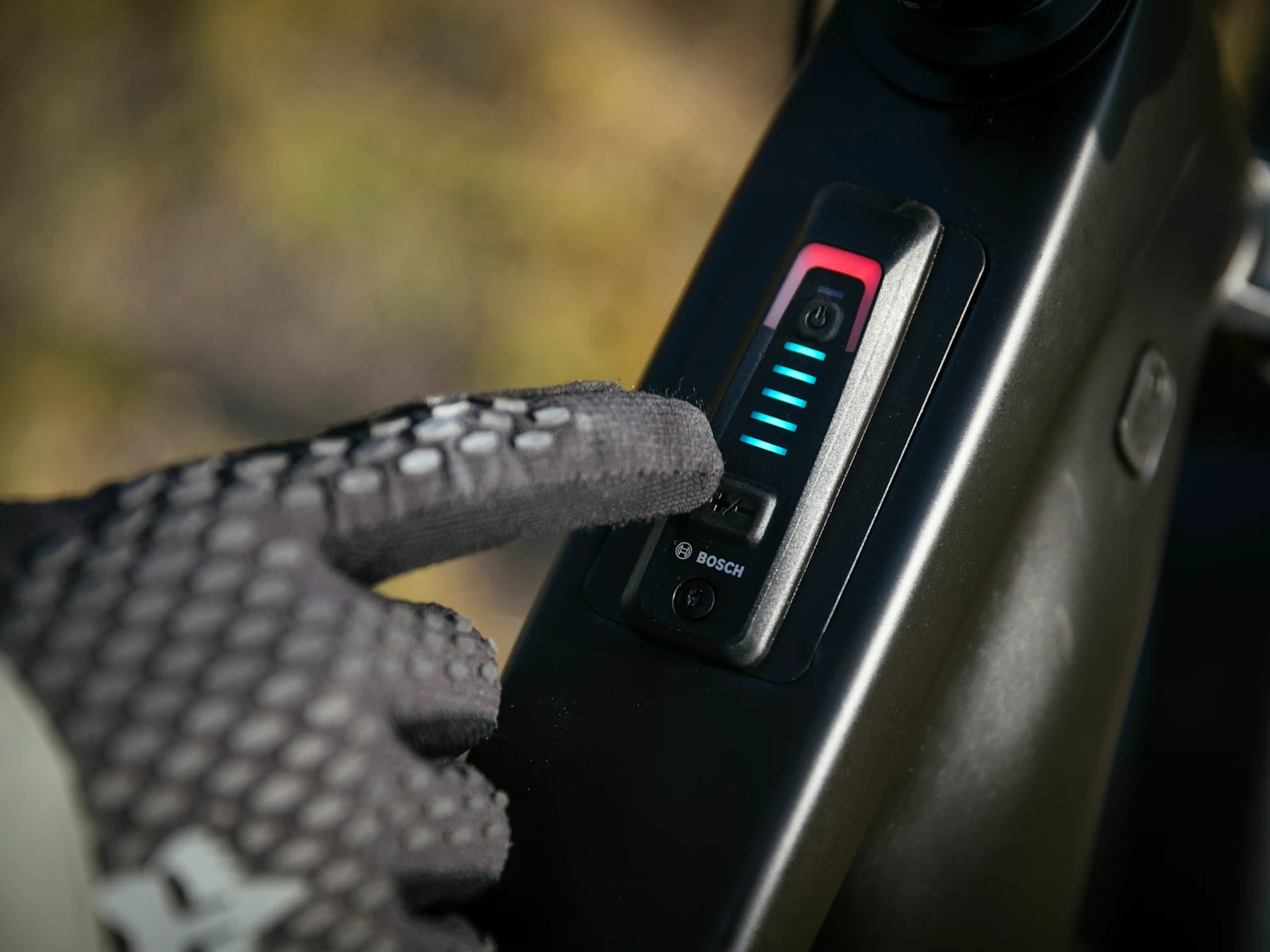 Nahaufnahme einer behandschuhten Hand, die das Bosch-Bedienfeld eines Trek Rail E-Mountainbikes berührt.