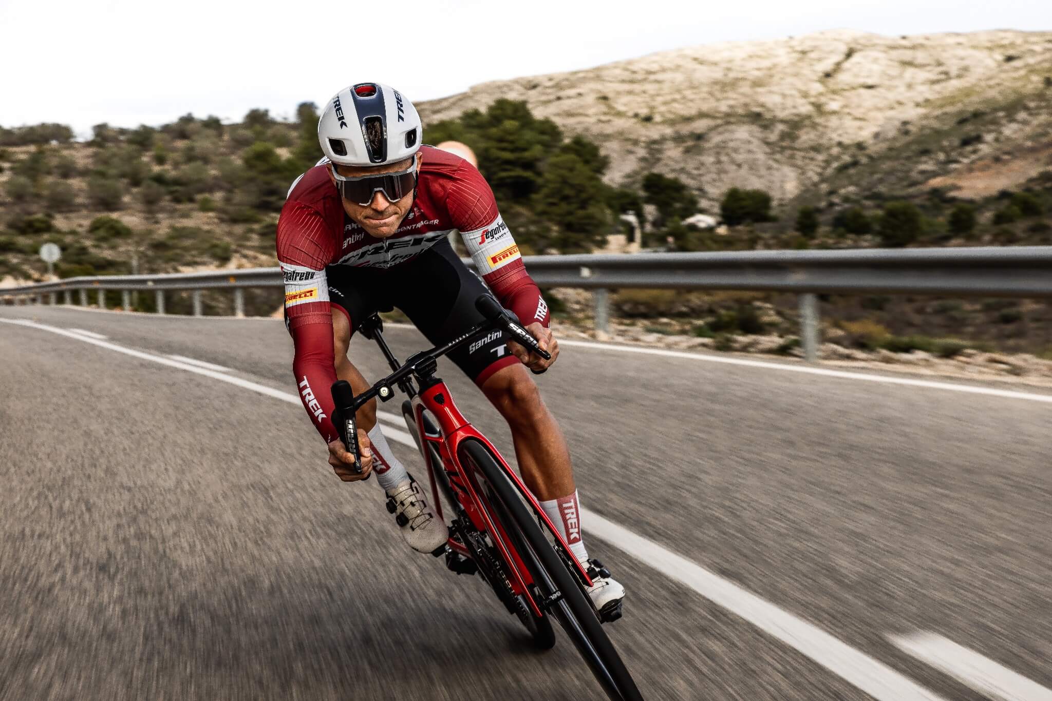 Radfahrer in roter Trek-Rennkleidung auf einem Trek Émonda Rennrad, fährt eine kurvenreiche Straße entlang.