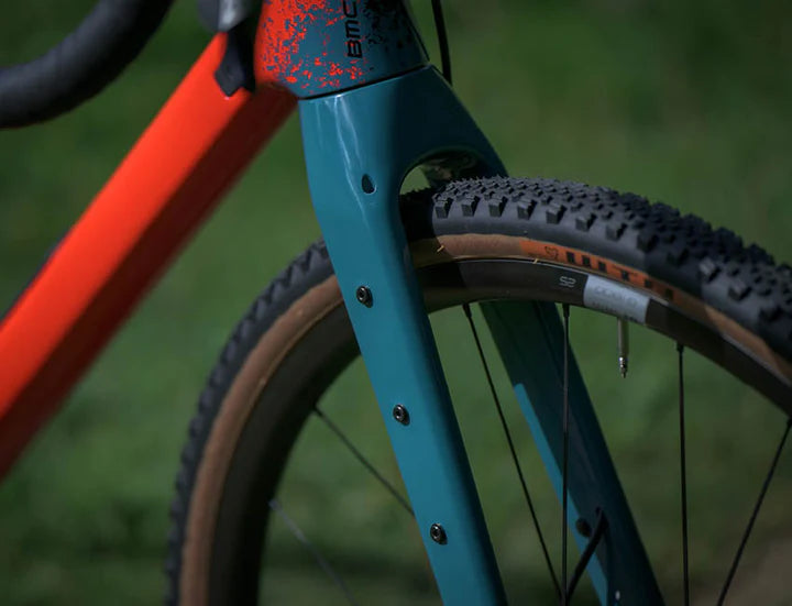 Nahaufnahme eines BMC URS Fahrrads mit breiten Reifen und zweifarbiger Lackierung in Orange und Blaugrün, ideal fürs Gelände.