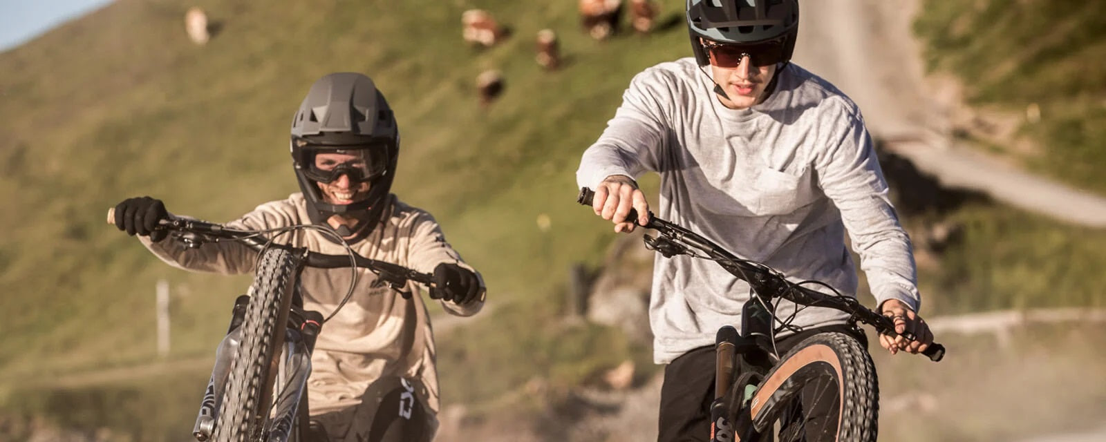 Zwei Personen mit Alpina-Helmen beim Mountainbiken in einer bergigen Landschaft, tragen sportliche Kleidung.