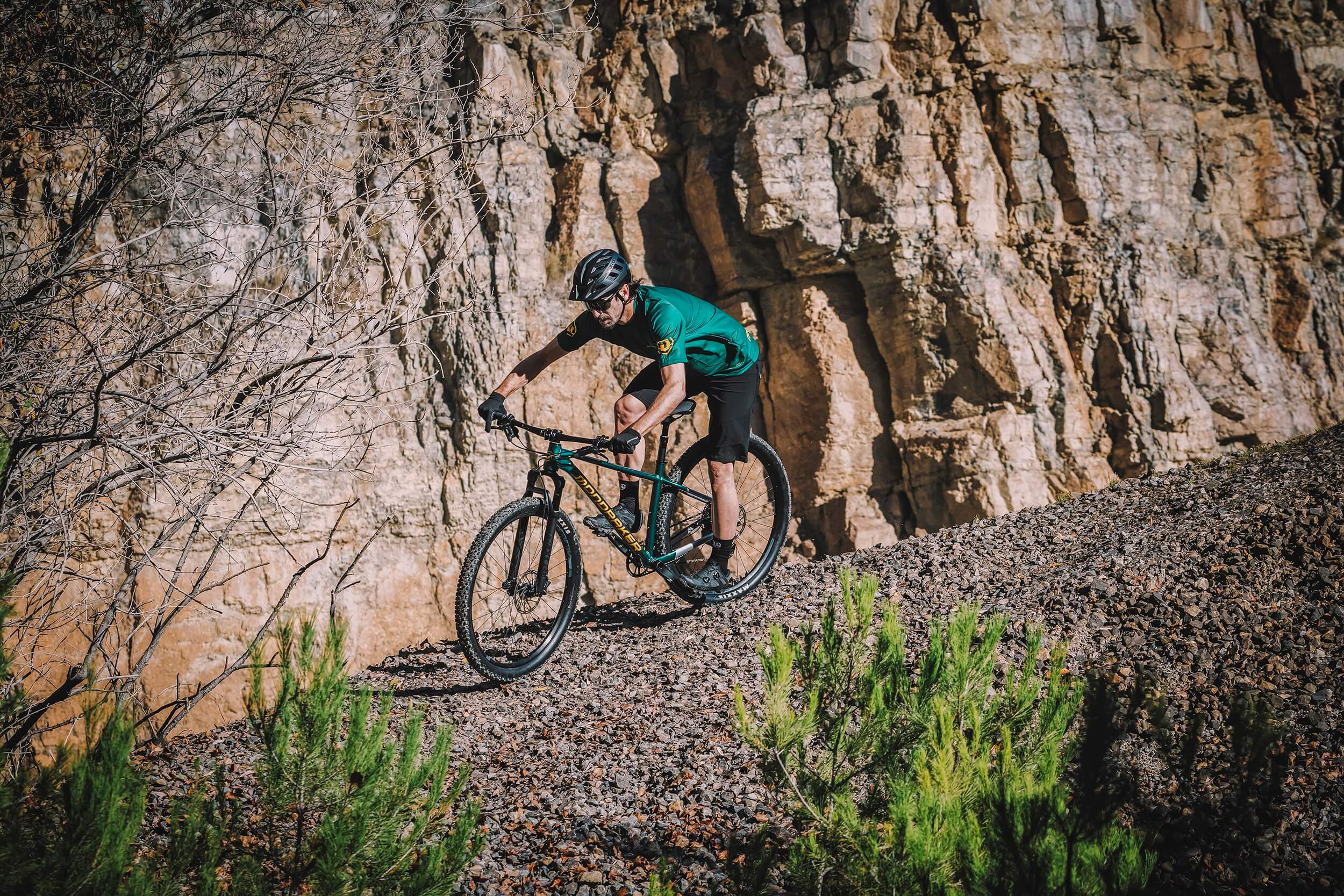 Mondraker Mountainbike im Gelände, Fahrer mit Helm und Schutzkleidung auf einem Schotterweg vor Felswand.