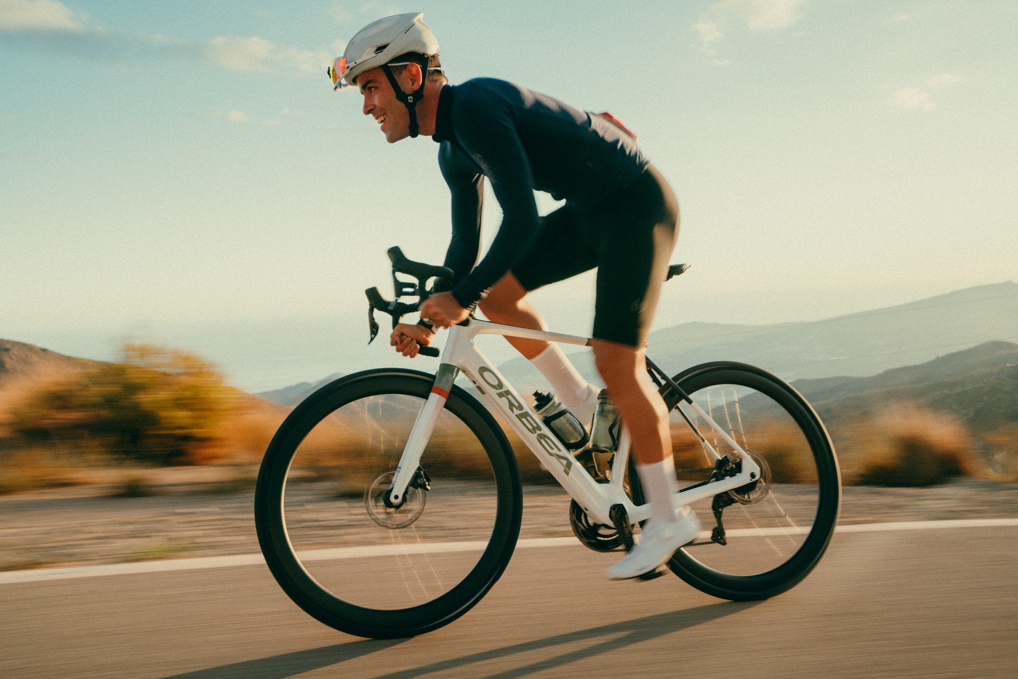 Radfahrer auf Orbea E-Bike auf offener Straße, bergige Landschaft, geeignet für sportliche Touren.