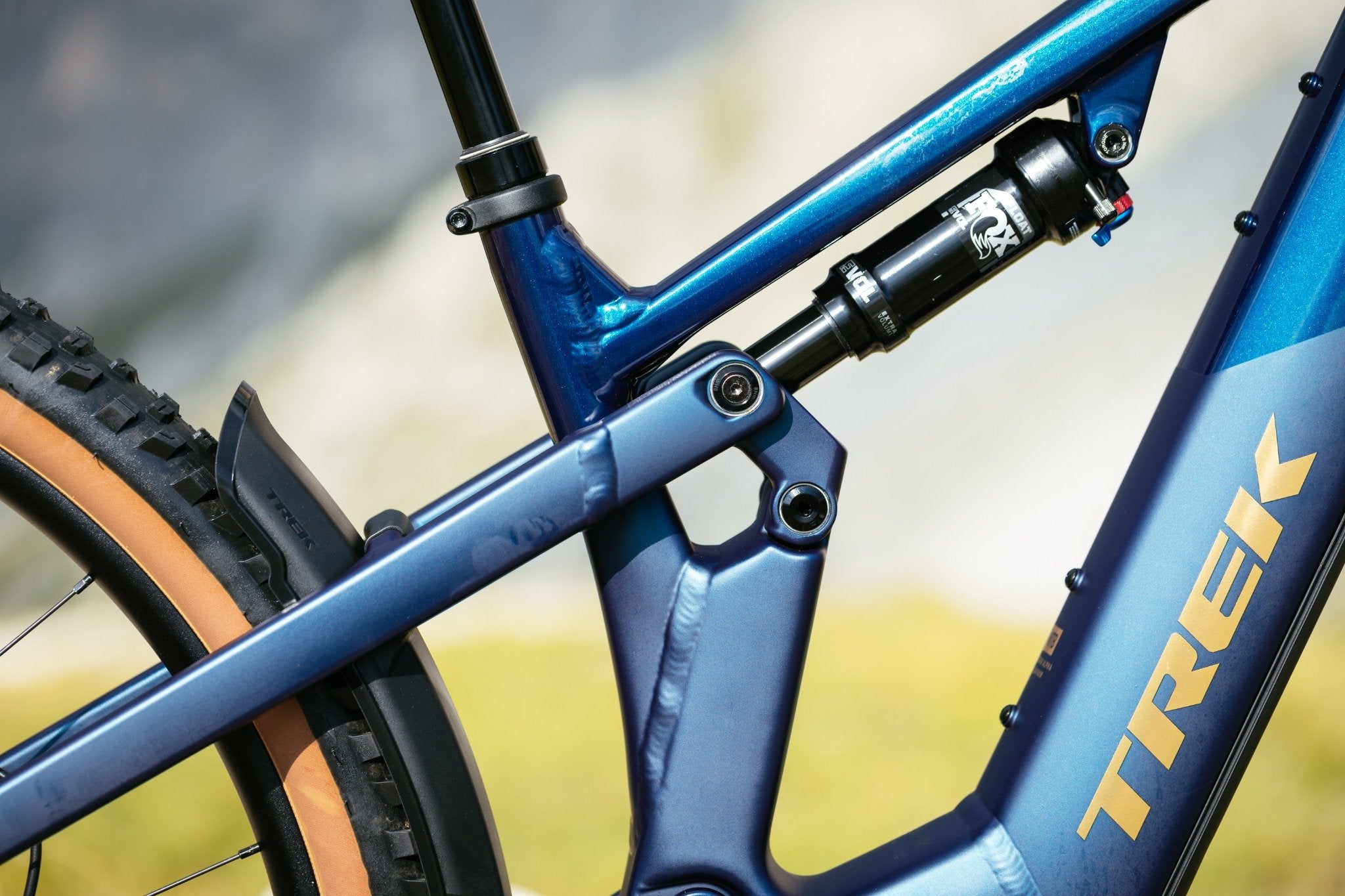 Nahaufnahme eines blauen Trek Powerfly FS Mountainbikes mit orange-schwarzen Reifen und FOX-Federung.