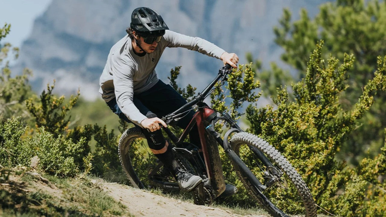 Person fährt ein Bosch E-Mountainbike abseits der Straße, trägt Helm und Schutzkleidung in bergiger Landschaft.