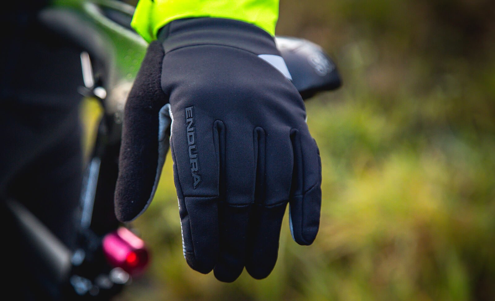 Schwarze Endura-Handschuhe für Radsport, getragen von Person in leuchtend gelber Jacke, Fahrrad im Hintergrund.