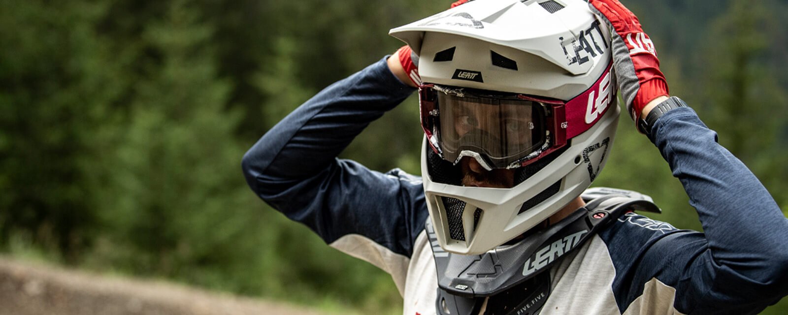 Person mit Leatt-Motocrosshelm und Schutzbrille im Wald, trägt roten Handschuh und Nackenschutz.