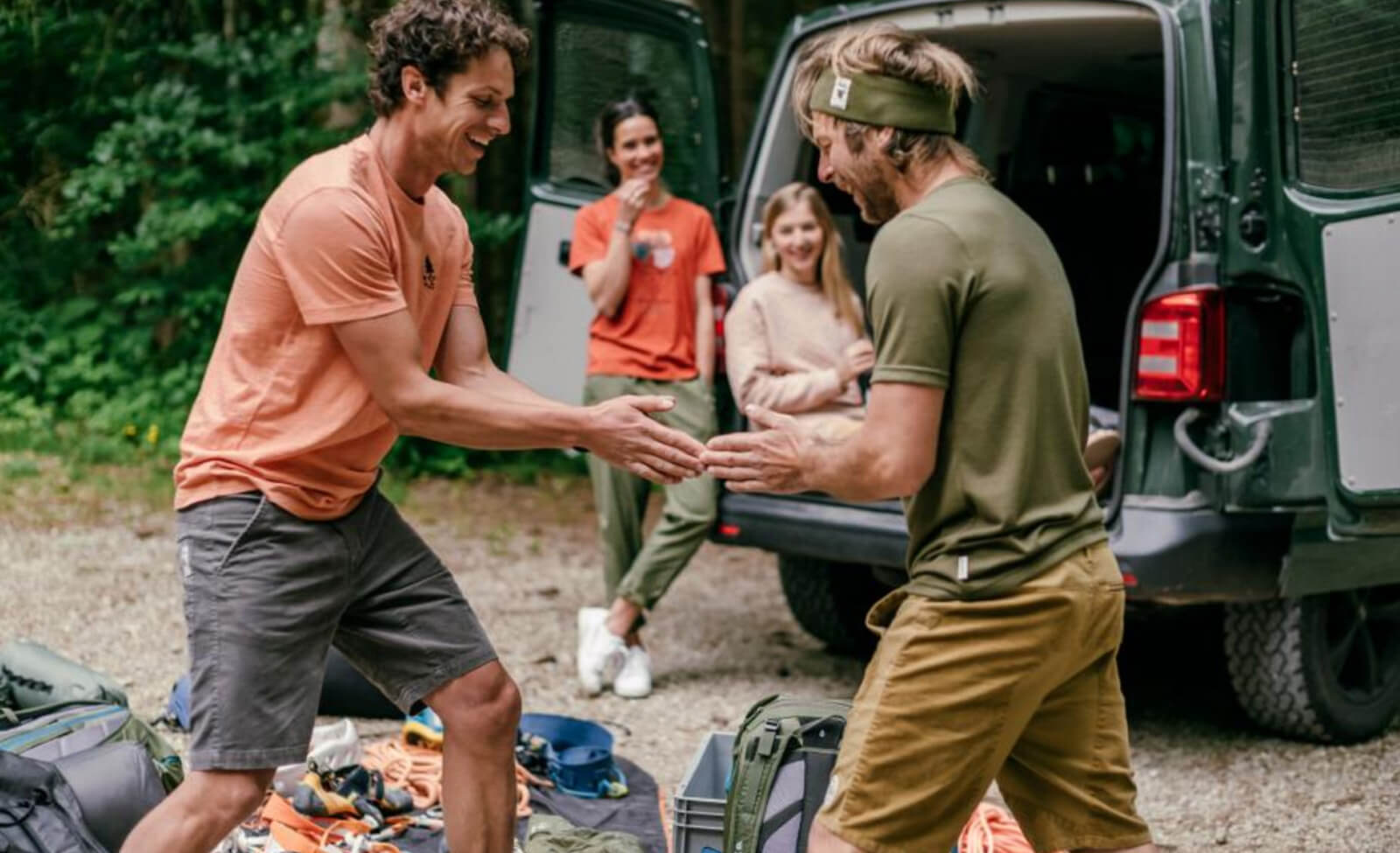 Gruppe von vier Personen bei Outdoor-Aktivitäten neben einem Van, lächelnd und fröhlich im freien Gelände.