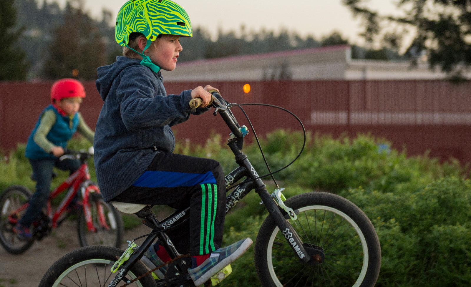 Zwei Kinder beim Radfahren, eines trägt einen grünen Helm, auf X-Games BMX-Rädern, draußen im Park.
