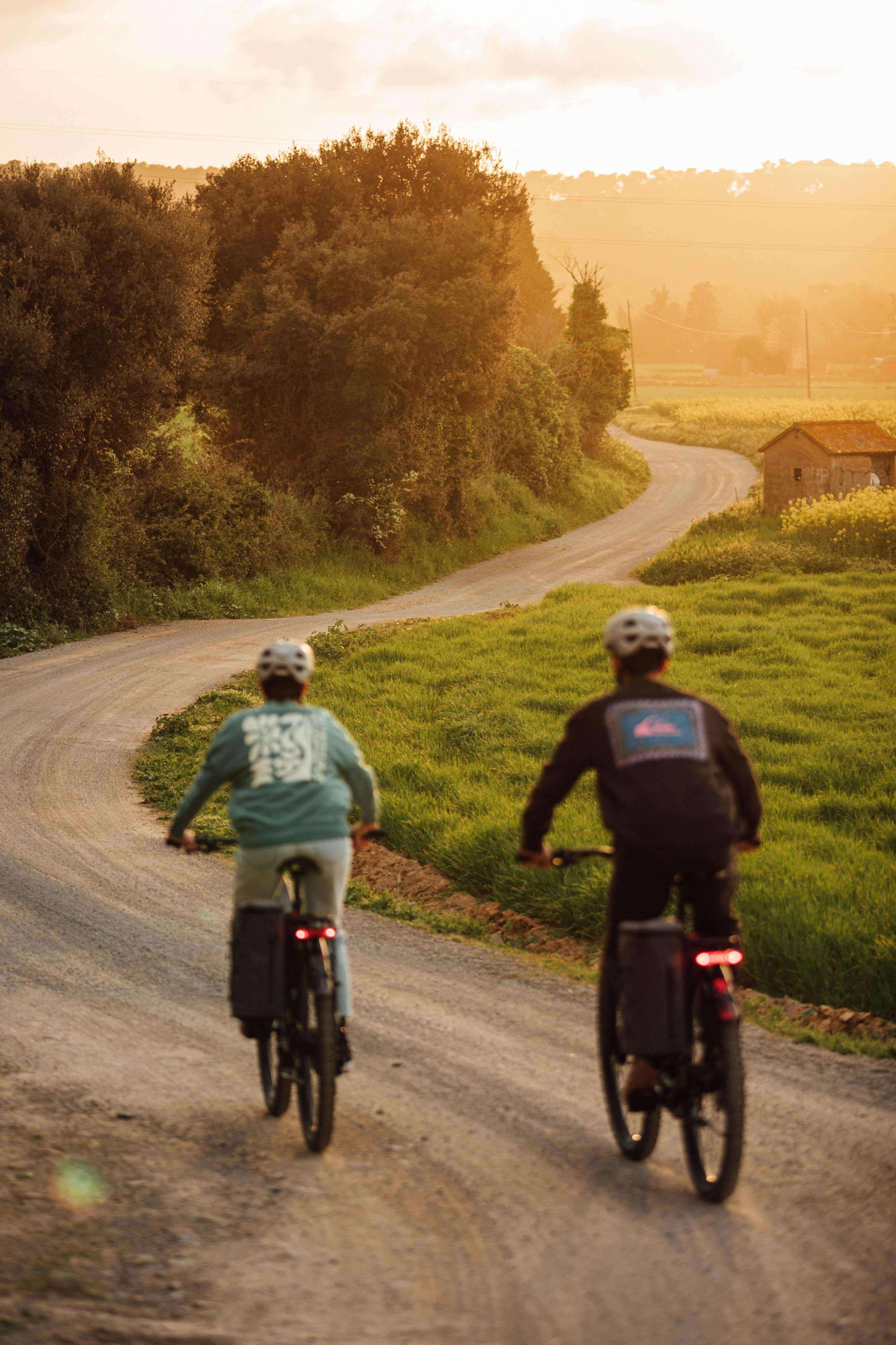 Zwei Personen fahren Orbea Kemen E-Bikes auf einem ländlichen Weg bei Sonnenuntergang.