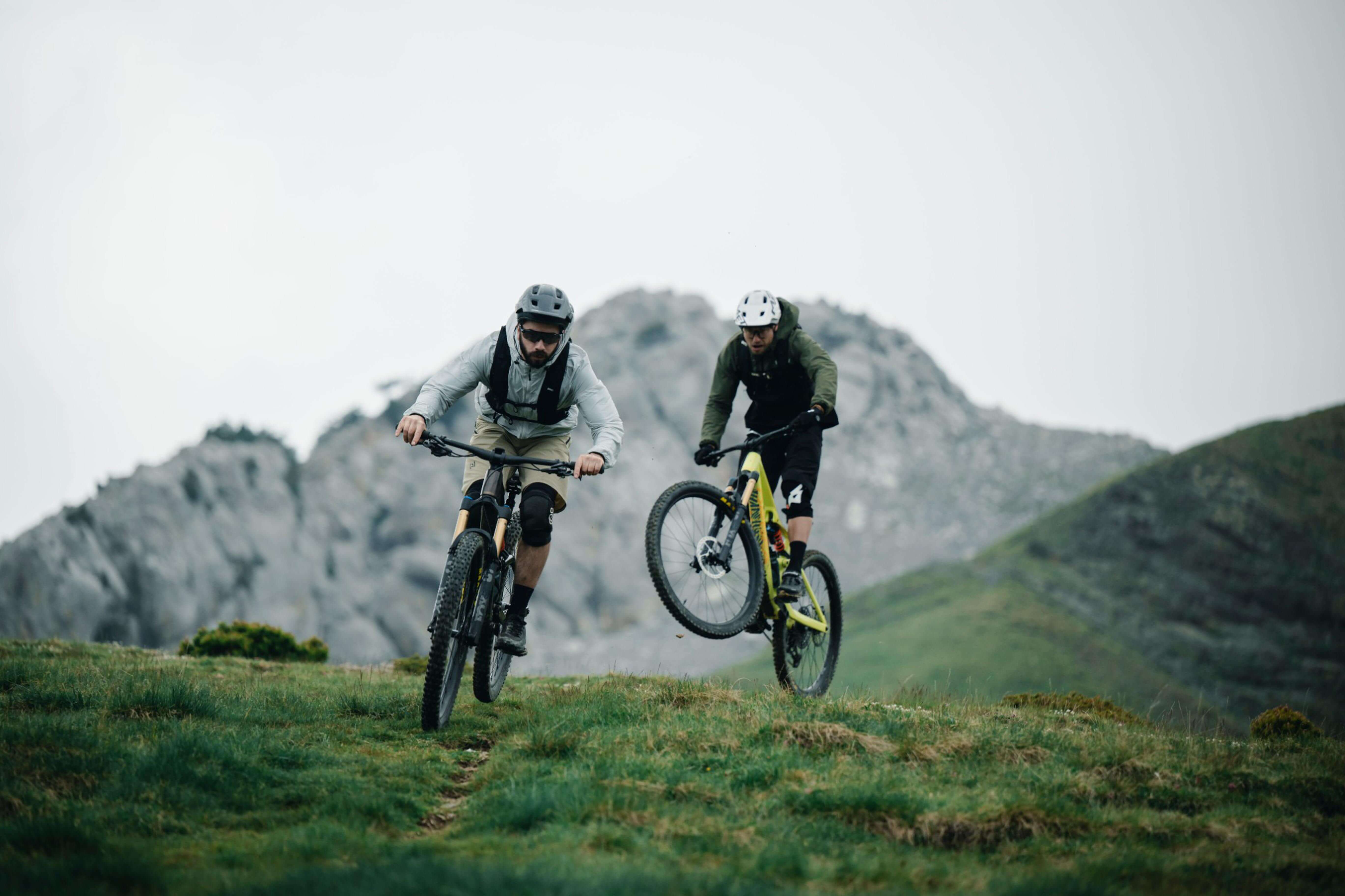 Zwei Mountainbiker fahren im Gelände mit Orbea Fully Fahrrädern vor einer Bergkulisse.