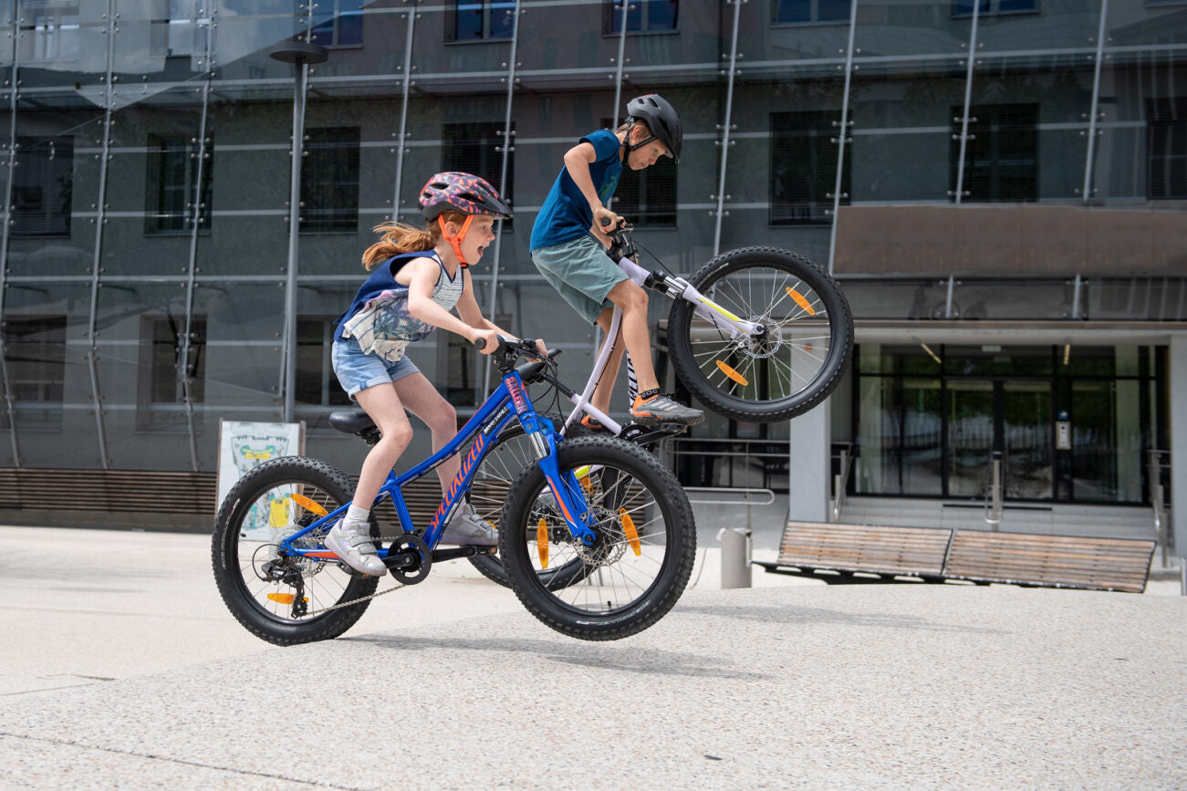 Kinder fahren Specialized-Fahrräder und springen in Freizeitkleidung und Helmen, ideal für junge Radfahrer.