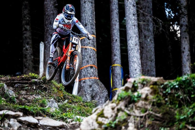 Mountainbiker auf Santa Cruz Fahrrad springt über Hindernis im Wald, geeignet für professionelle Downhill-Rennen.