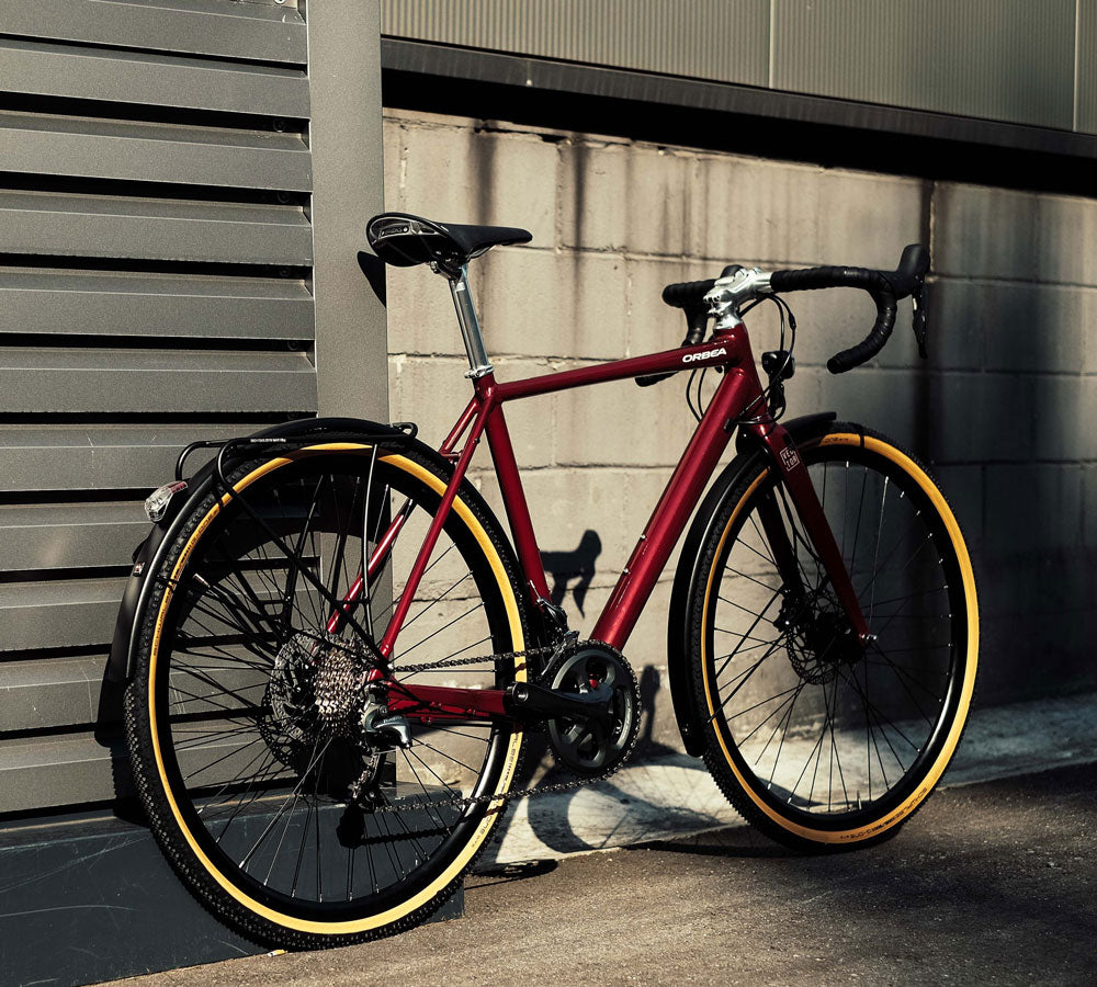 Rotes Orbea-Fahrrad mit Rennradlenker und gelben Reifen, lehnt an einer Mauer; geeignet für sportliche Touren.