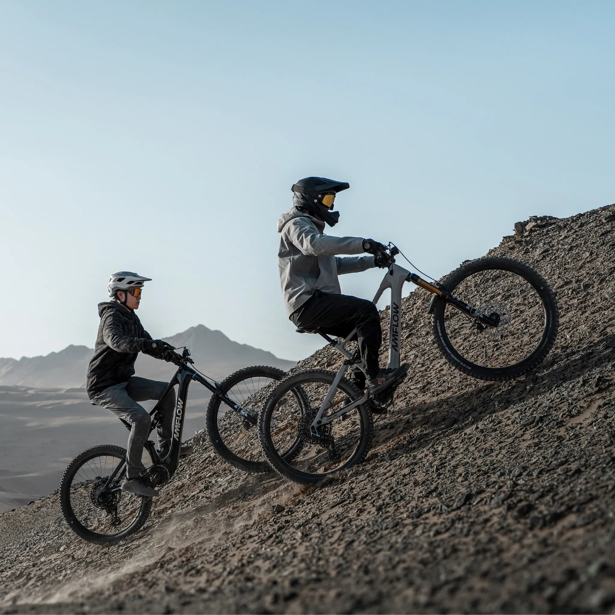 Zwei Personen fahren mit Amflow E-Bikes einen steilen Schotterhang hoch, ausgestattet mit Helmen und spezieller Kleidung, sowie den Avinox M2S Motor .