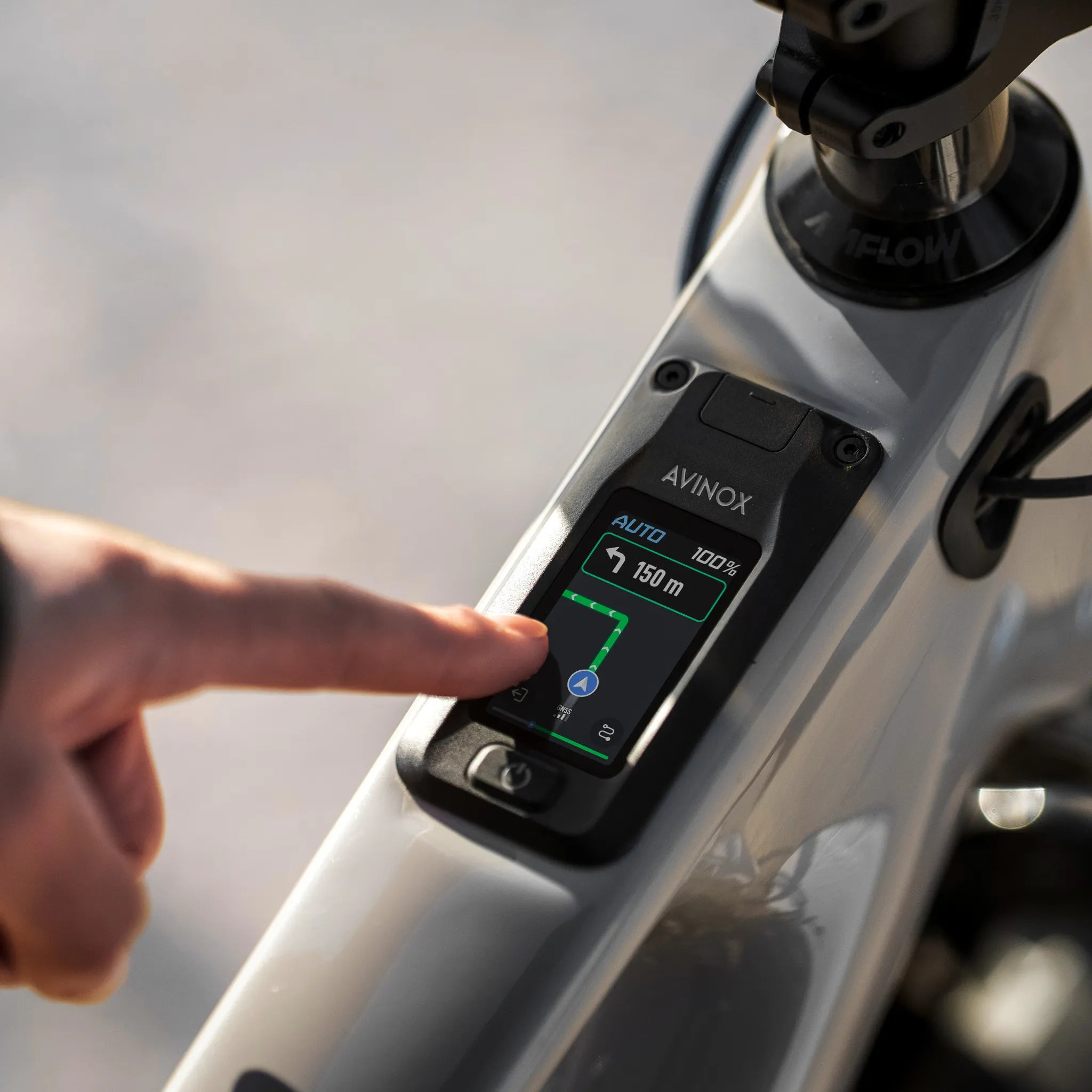 Nahaufnahme eines E-Bike-Displays von Avinox mit Navigation, Hand tippt auf Bildschirm, geeignet für moderne Radfahrer.