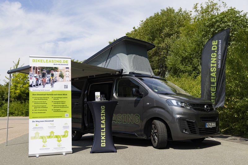 Messestand mit Opel-Van, Sonnendach und "BIKELEASING.DE"-Banner. Präsentation von Dienstrad-Leasing-Angeboten im Freien.