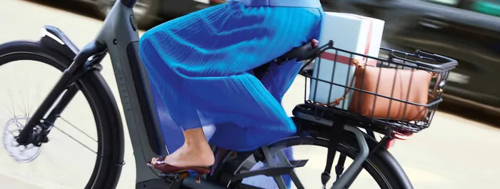 Frau auf einem Gazelle Bike mit Korb, darin eine Tasche und Box, fährt auf Straße. Bequeme Fortbewegung in der Stadt.
