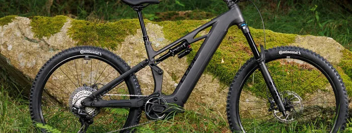 Schwarzes Cube Stereo Hybrid One77 mit Federung und Continental-Reifen, im Grünen vor einem moosbedeckten Felsen platziert.