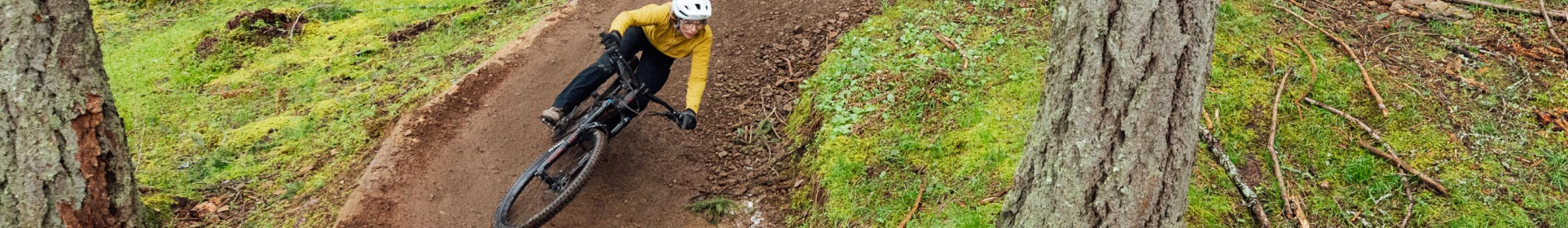Radfahrer auf einem Specialized Turbo Levo SL E-Mountainbike in der Kurve eines Waldtrails, trägt gelben Pullover und Helm.