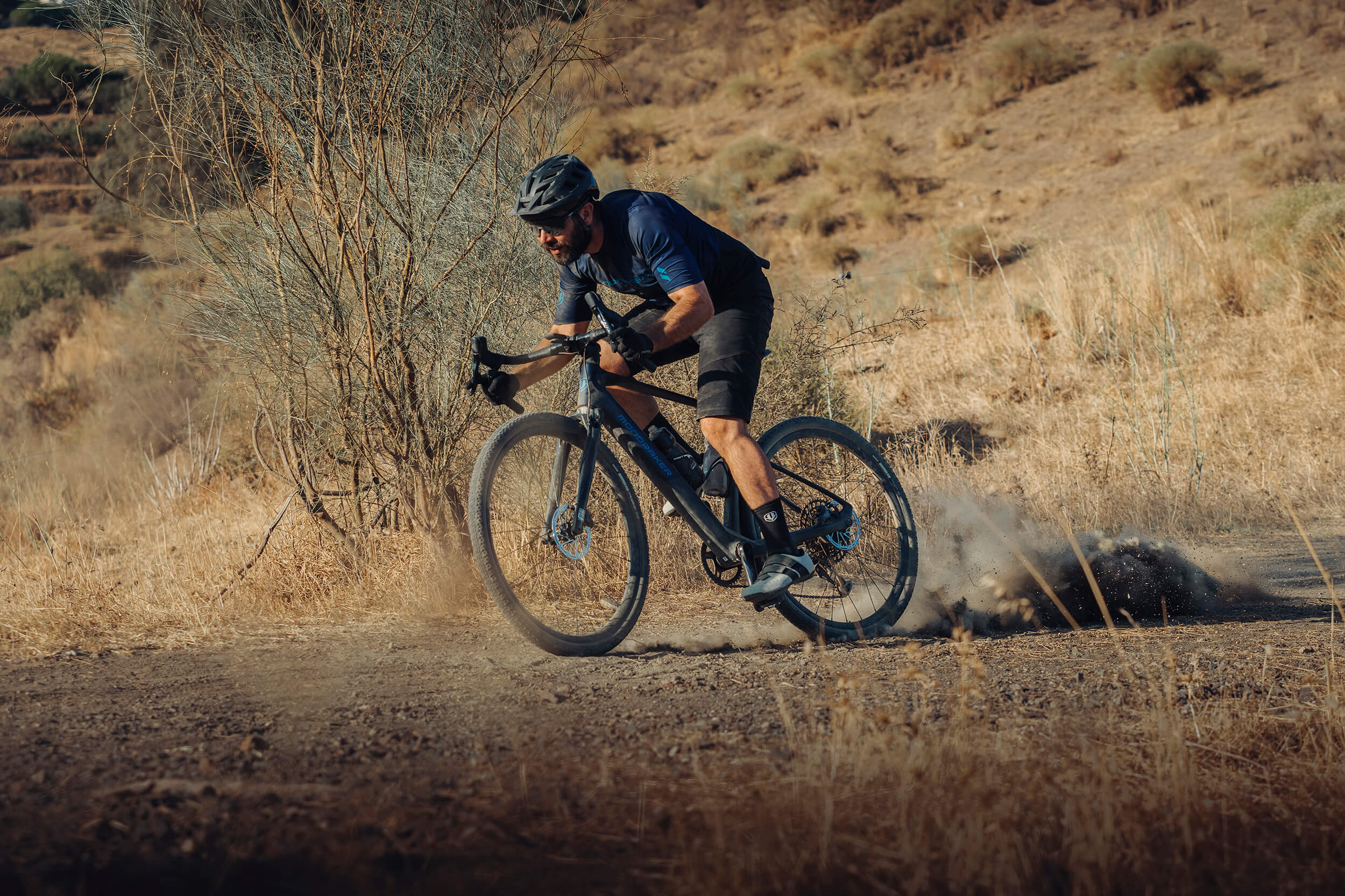 Mann fährt Mondraker E-Gravel Bike auf staubigem Weg in trockener Landschaft. Ideal für Offroad-Abenteuer.