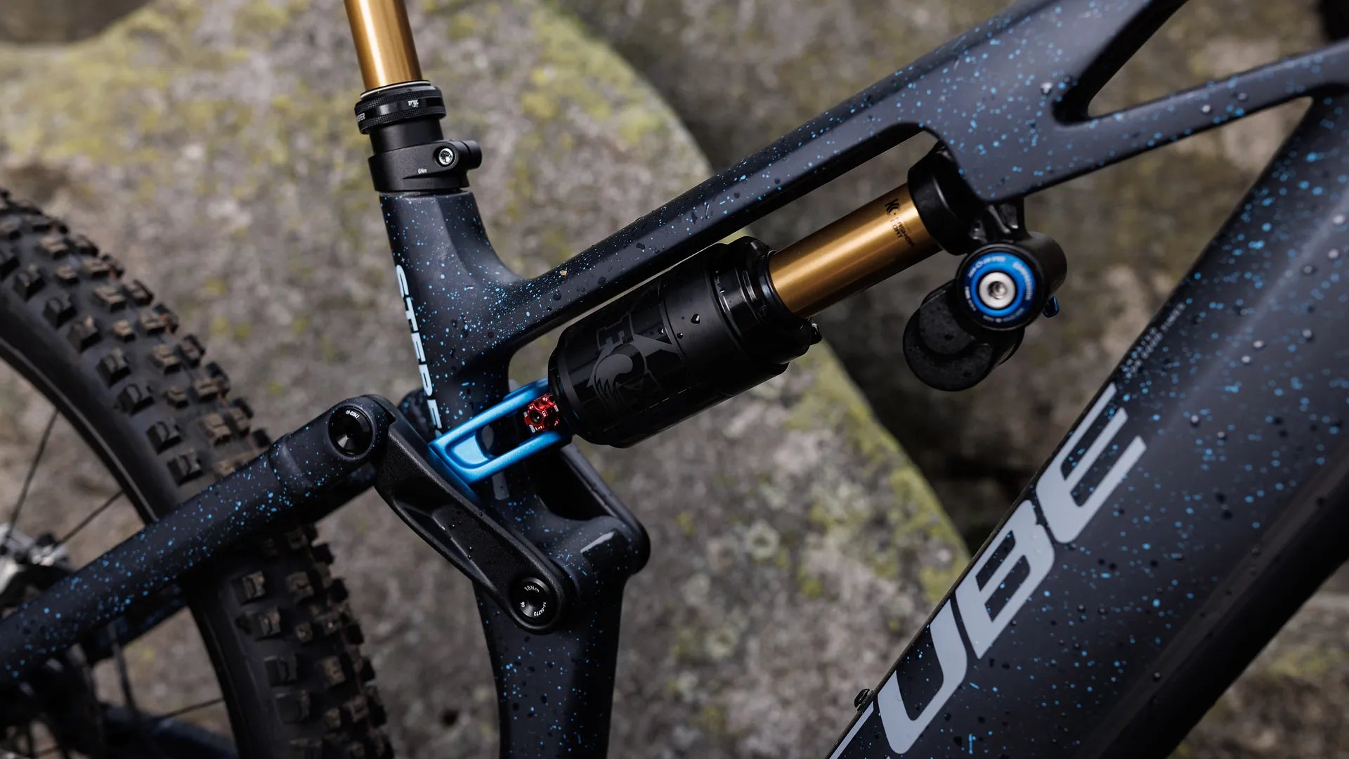 Detail eines CUBE STEREO HYBRID ONE77 HPC SLT 800
-Rahmens mit Federung, geeignet für Offroad-Fahrten, auf steinigem Hintergrund.